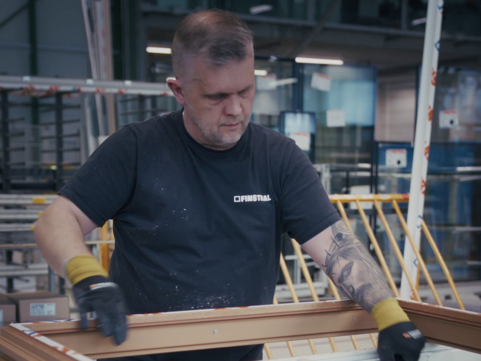 Mitarbeitende Person mit Arbeitshandschuhen bei der Bearbeitung eines Fensterrahmens in der Finstral-Produktion.